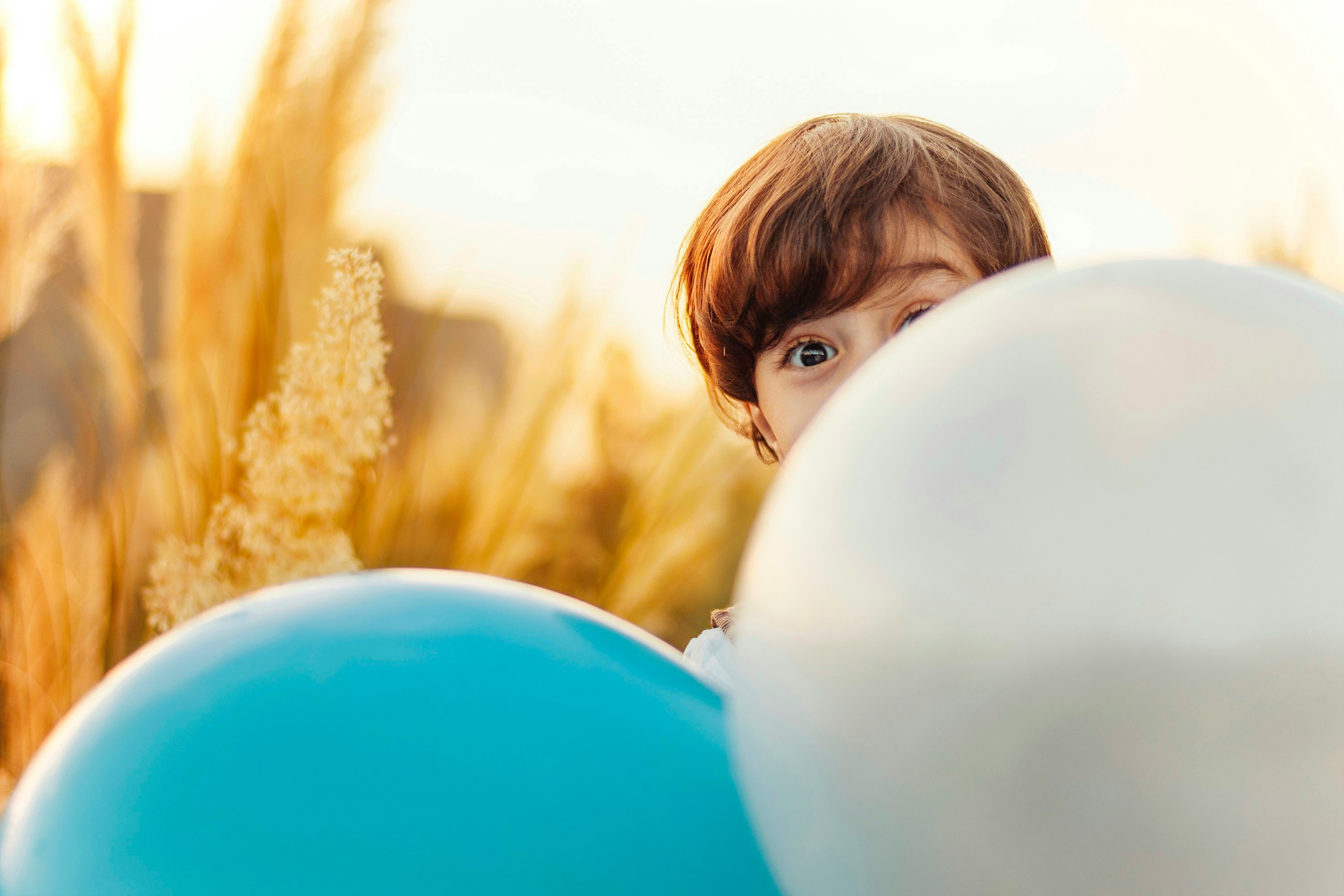 En gutt som gjemmer seg bak to ballonger